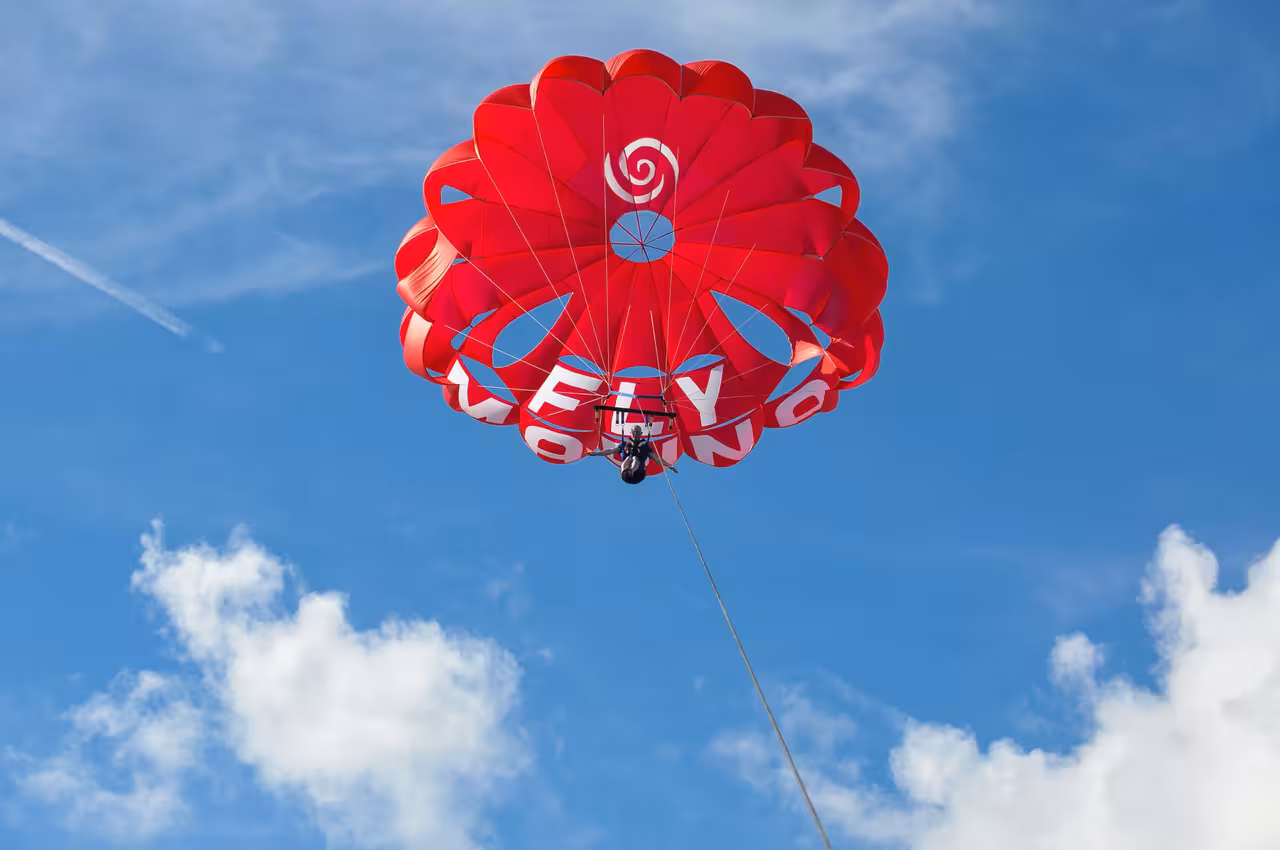 Vibrant red parasail canopy soaring high against a blue sky on a guided parasailing tour over Albufeira Algarve Portugal