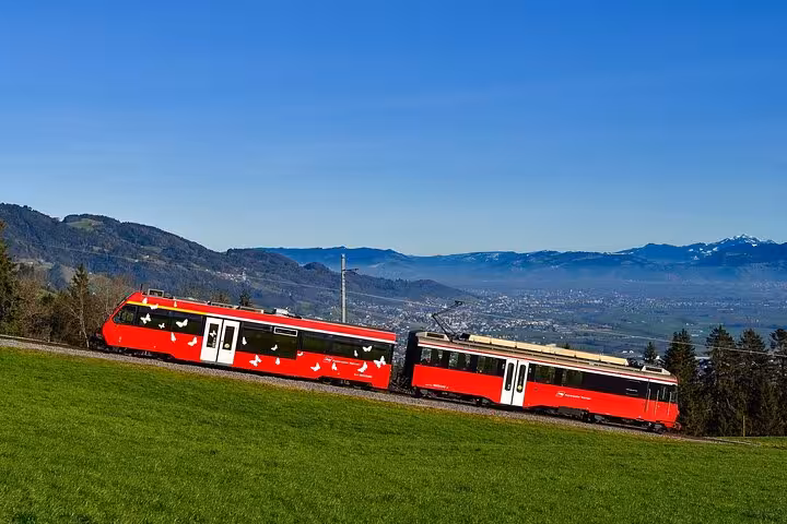 Red scenic train traverses lush landscapes in St. Gallen, offering breathtaking views of Swiss countryside.
