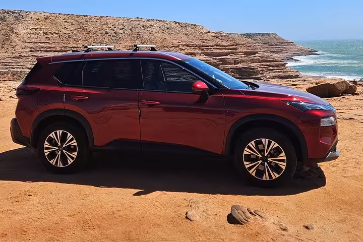 Red SUV parked on rugged terrain with ocean views during the Pinnacles segment of the 2 Days One Night Tour.