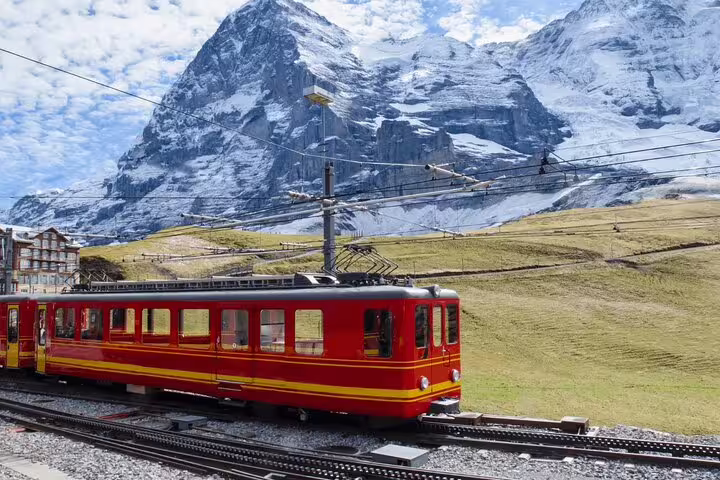 Red train on the scenic route to Jungfraujoch with stunning views of snow-capped Swiss Alps in the background.
