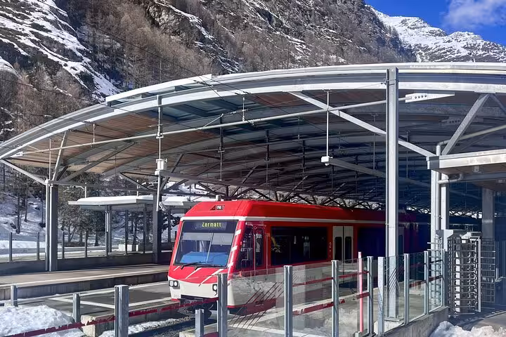 Red train at Zermatt station with snowy mountains, highlighting travel from Milan to Zermatt Tasch.