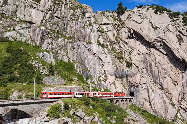 Red train traveling through rocky terrain in the Swiss Alps on a scenic railway tour.