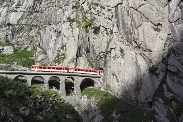 Red train navigating a historic stone viaduct through rugged Swiss Alps, a highlight of scenic rail tours.