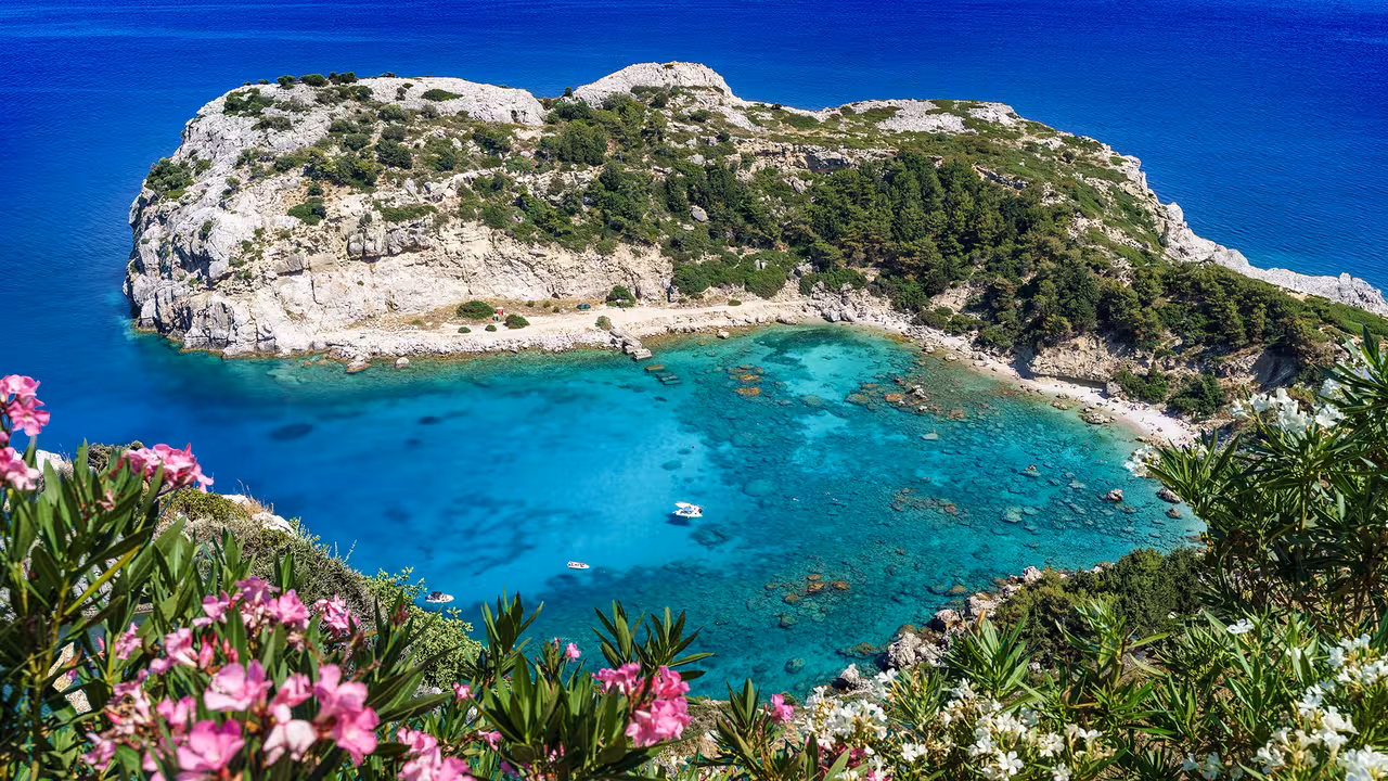 Aerial view of a stunning turquoise bay surrounded by rocky cliffs and vibrant flowers at Regal 2700 tour location.