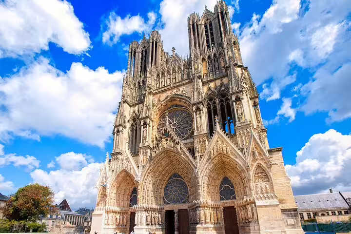 Majestic Reims Cathedral under blue sky, a highlight on the Private Champagne Day Trip from Paris, showcasing Gothic architecture.