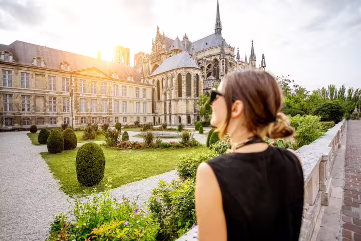 A visitor enjoys the scenic view of historic Reims Cathedral gardens during a private Champagne day trip from Paris with lunch.