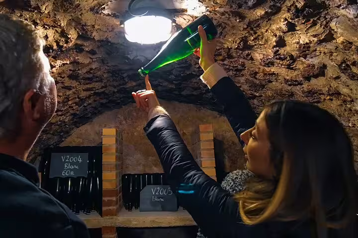 Tourists explore a wine cellar in Reims, examining a champagne bottle during a private day trip with French lunch from Paris.