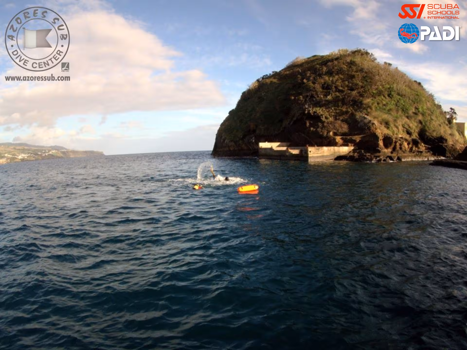 Rescue Diver training in open water near rocky Azores coastline with surface marker float and waves