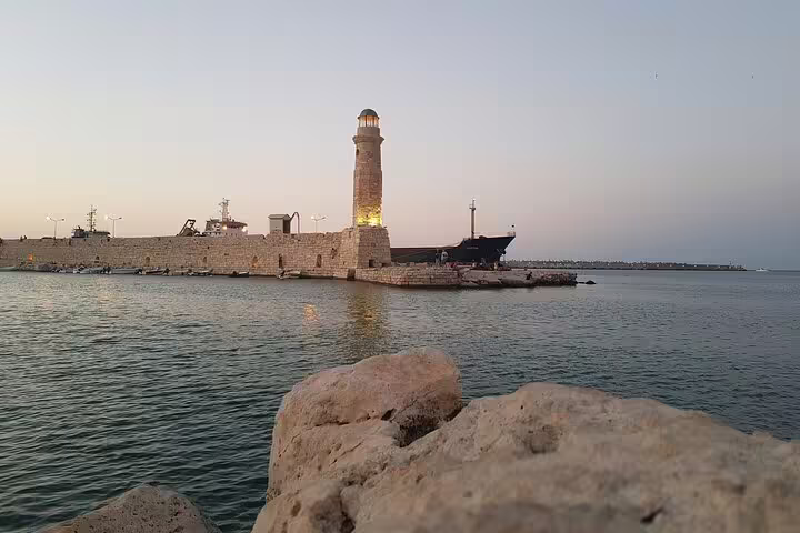 Scenic sunset at Rethymno's historic lighthouse and harbor, highlighting the tranquil sea and ancient architecture.