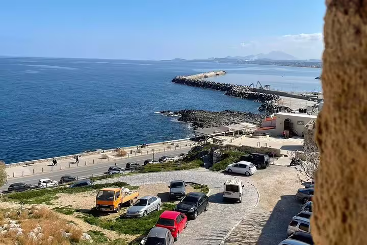 Scenic coastal view of Rethymno port with parked cars and a clear blue sea, ideal for exploring Crete on a private tour.