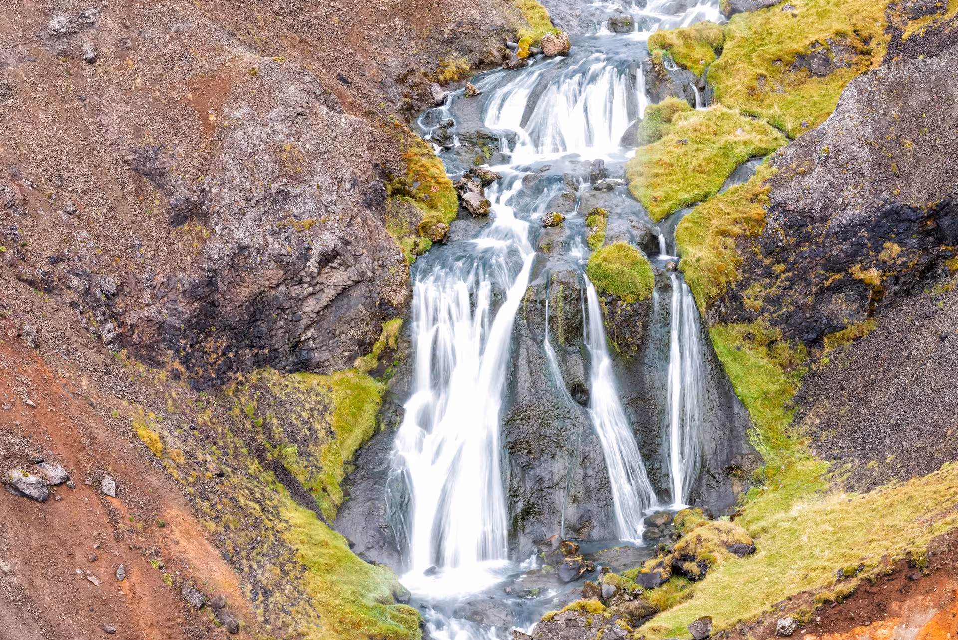 Small waterfall in Reykjadalur valley on private Grændalur circle hike, mossy lava rocks and stream