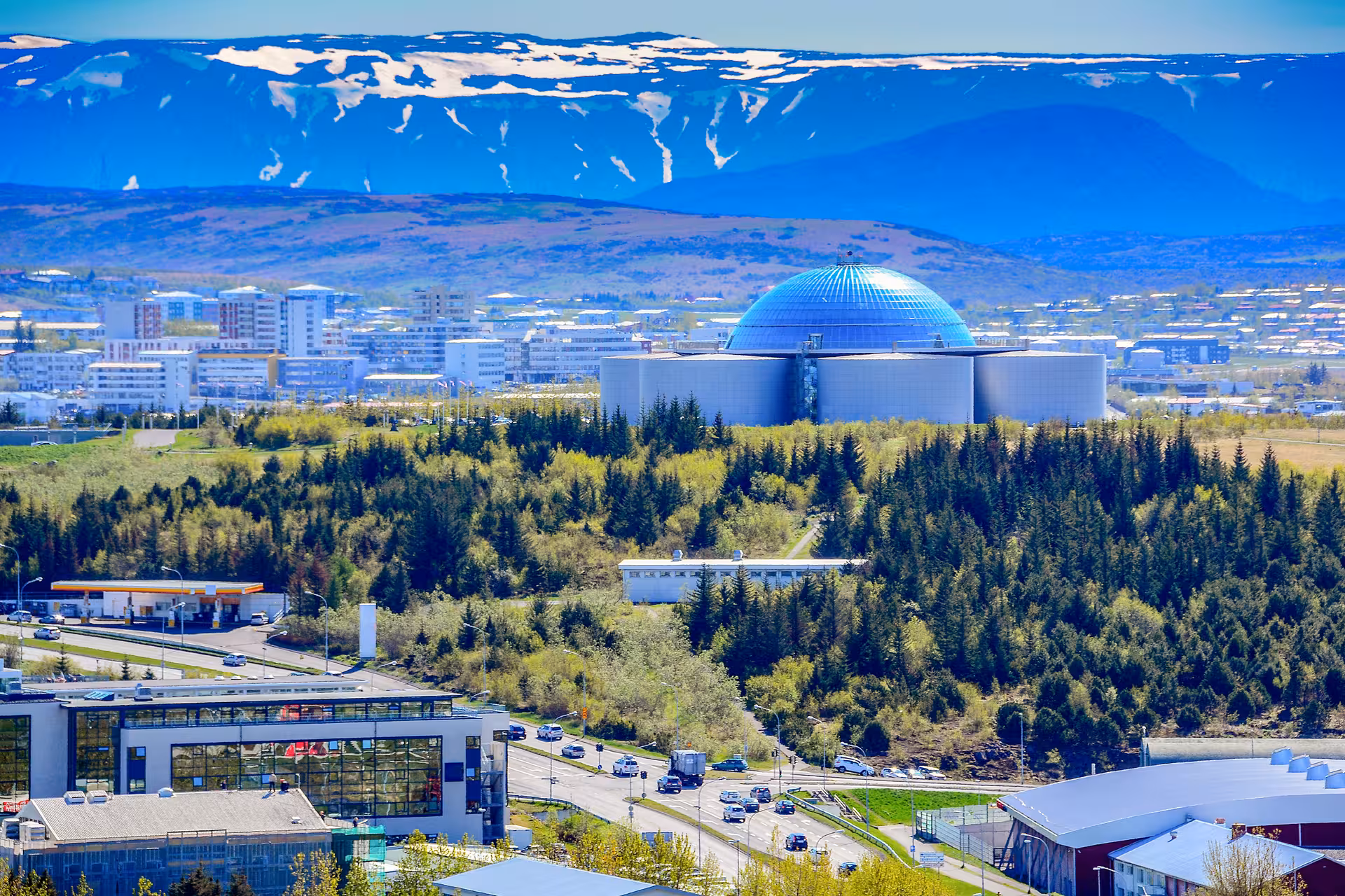 Panoramic view of Reykjavík with the iconic Perlan building and snow-capped mountains in the background.