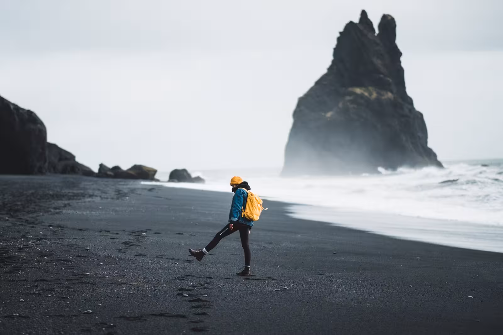 Traveler exploring Reynisfjara black sand beach along Iceland's south coast, iconic rock formations in the background.