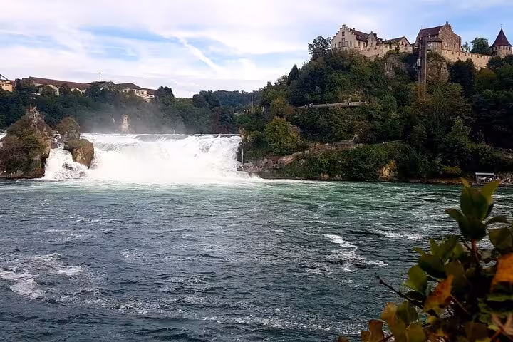 Breathtaking view of Rhine Falls with lush greenery and historic castle perched on the cliffs in Switzerland.