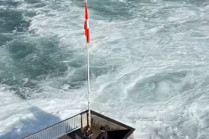 Viewing platform by roaring Rhine Falls with Swiss flag, highlight of a half day luxury tour from Zurich