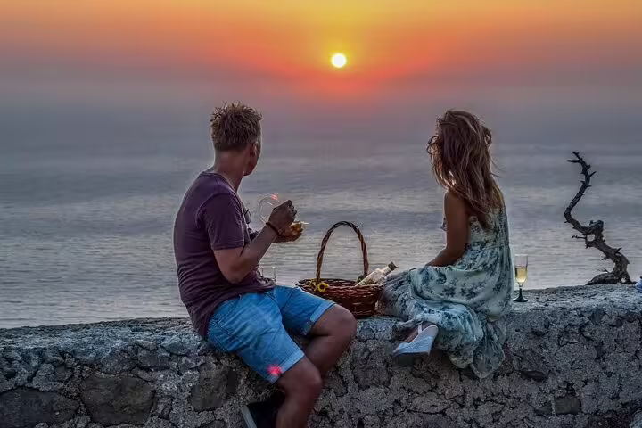 Couple enjoys a private wine tasting at sunset overlooking the sea in Rhodes, featuring a scenic drive and stunning views.