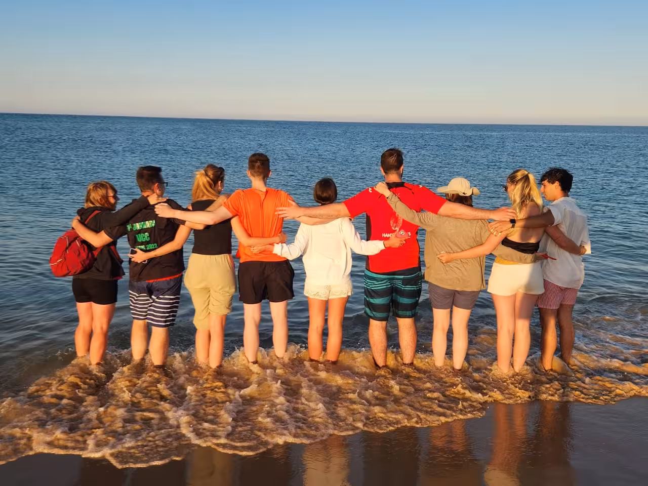 Group enjoying sunset on the beach after a Ria Formosa 2-hour tour, standing in the surf arm in arm