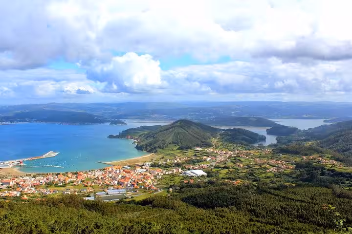 Picturesque coastal landscape of Rías Altas with vibrant villages and a serene bay under a partly cloudy sky.