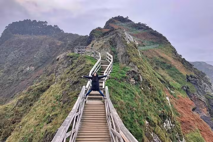 Traveler enjoying the scenic walkway at Fuciño do Porco, offering stunning panoramic views of lush green cliffs.