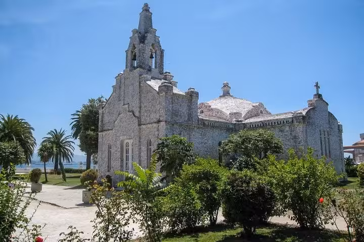 Historic stone church surrounded by lush gardens under a clear blue sky in Rias Baixas tour.