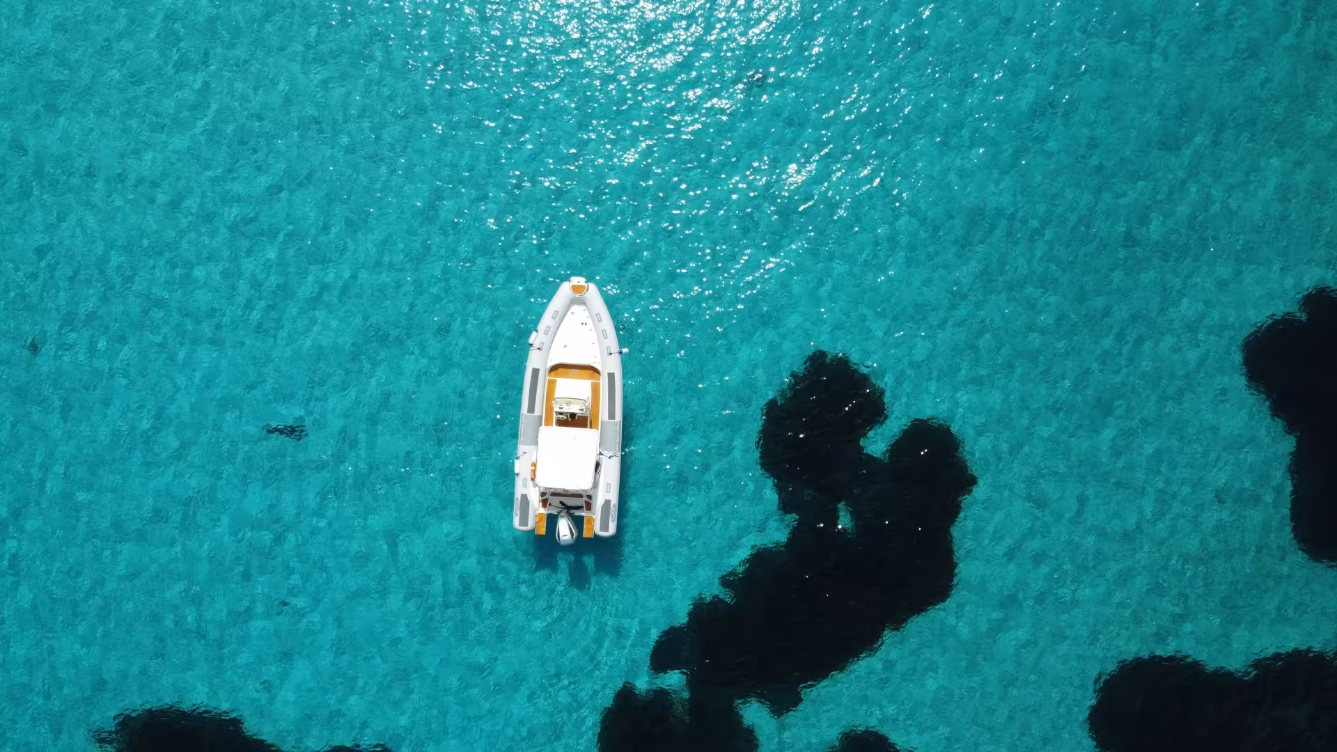 Close-up aerial shot of a RIB boat floating on the crystal-clear turquoise sea in the Gulf of Asinara, highlighting marine beauty.