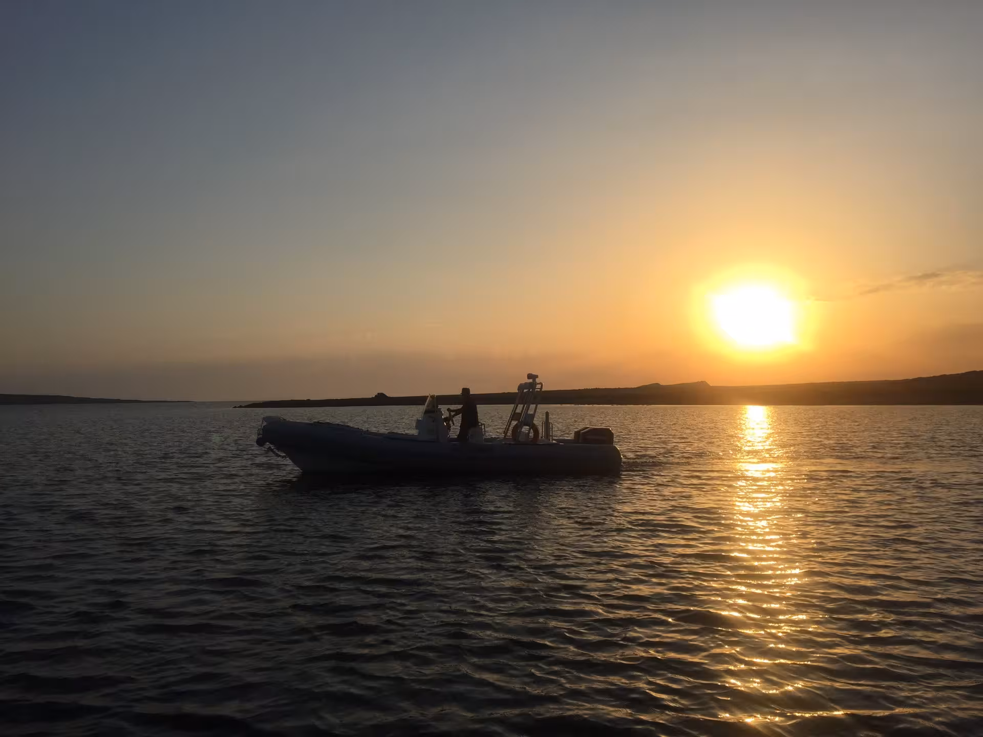 Silhouette of a RIB boat cruising during a stunning sunset in the Gulf of Asinara, creating a serene tourism experience.