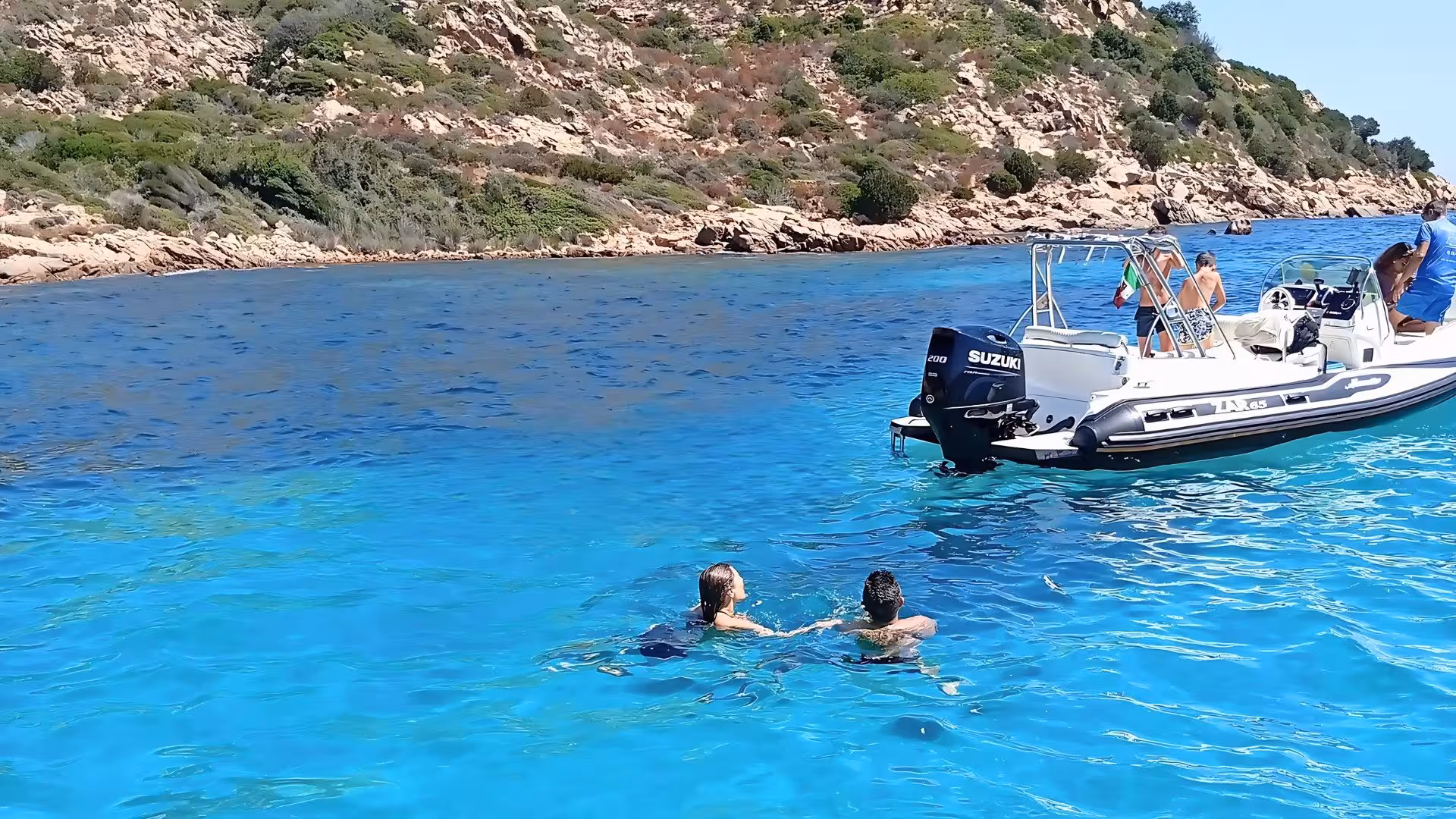 Tourists enjoy swimming near a RIB boat in the clear turquoise waters off Capriccioli on a sunny day.