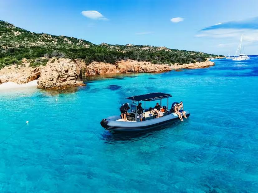 A RIB boat with tourists cruises the turquoise waters of La Maddalena Archipelago, showcasing Sardinia's stunning coastline.