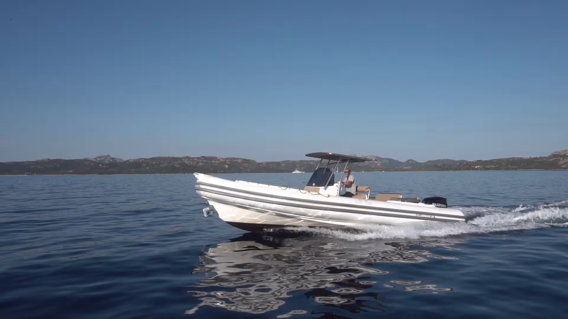 Side view of a RIB boat gliding across the serene waters with scenic La Maddalena landscapes in the background.