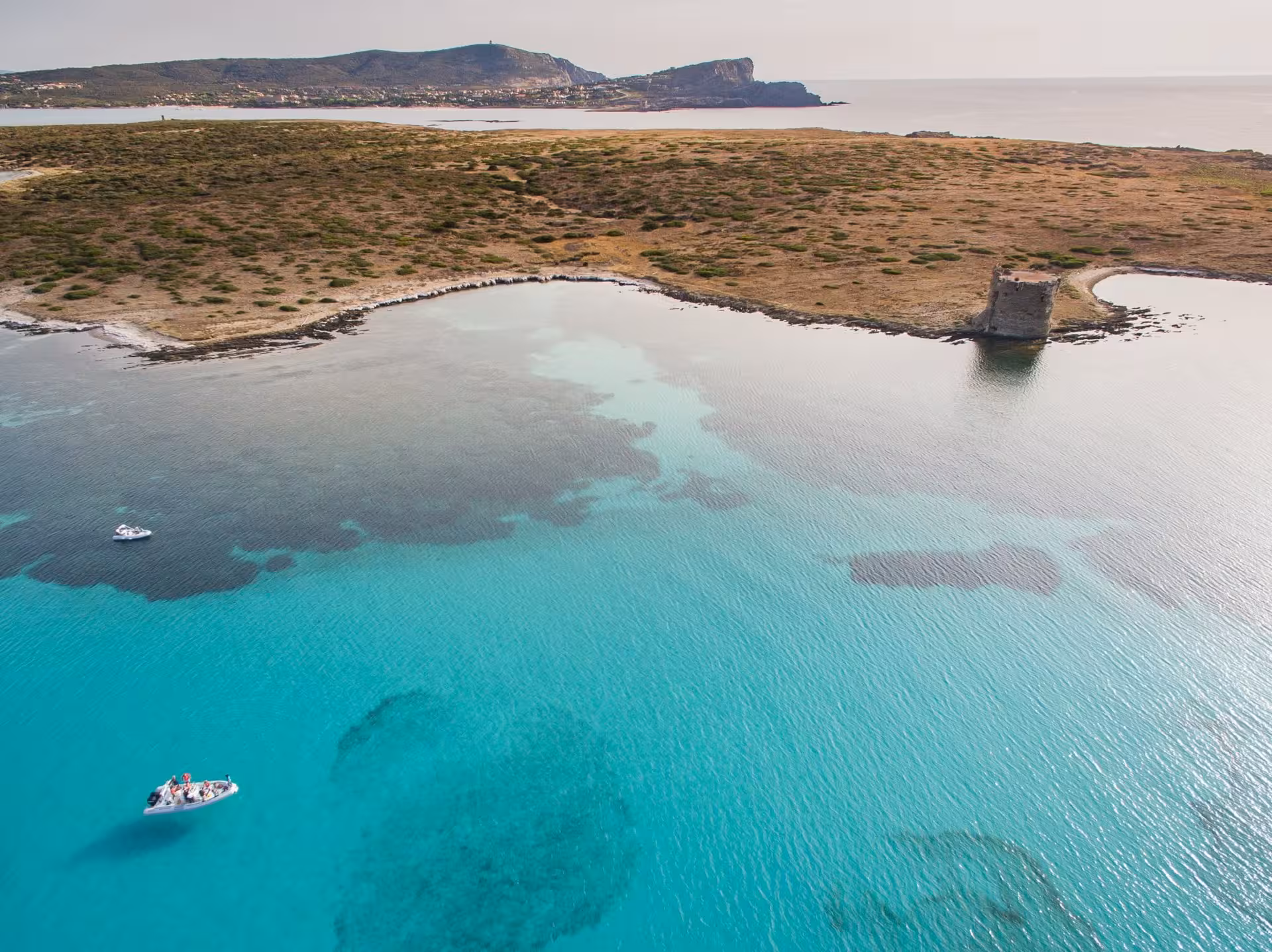 Aerial view of RIB boats exploring the turquoise waters of Asinara Gulf with a historic coastal tower in the background.
