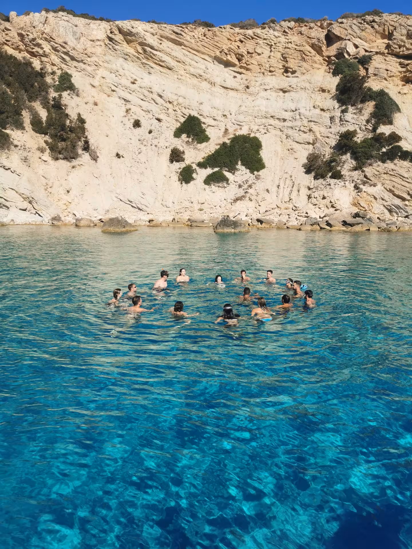 Group of swimmers enjoying the turquoise waters and rocky cliffs on a RIB tour to Carloforte.
