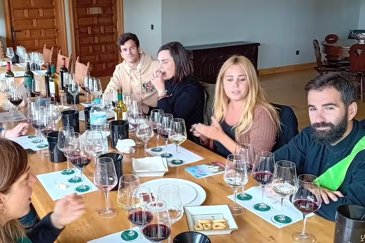 Guests enjoy wine tasting at Ribera del Duero winery, surrounded by glasses and bottles on a wooden table.