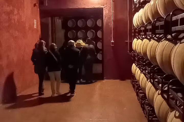 Visitors exploring a dimly lit wine cellar with stacked barrels at a Ribera del Duero winery tour from Madrid.
