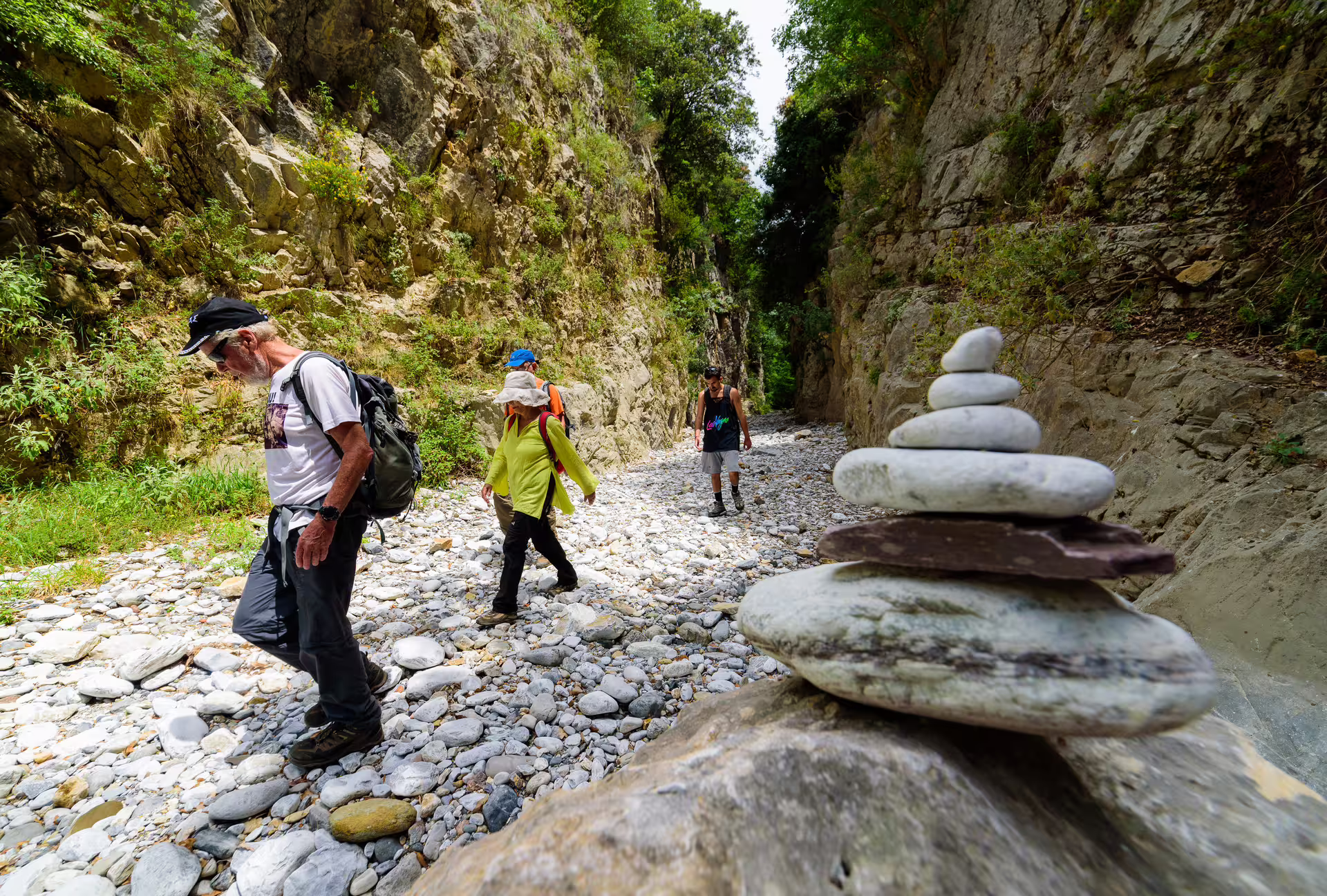 Group hiking through narrow Ridomo Gorge canyon with stacked river stones, on a guided Greece gorge trekking experience
