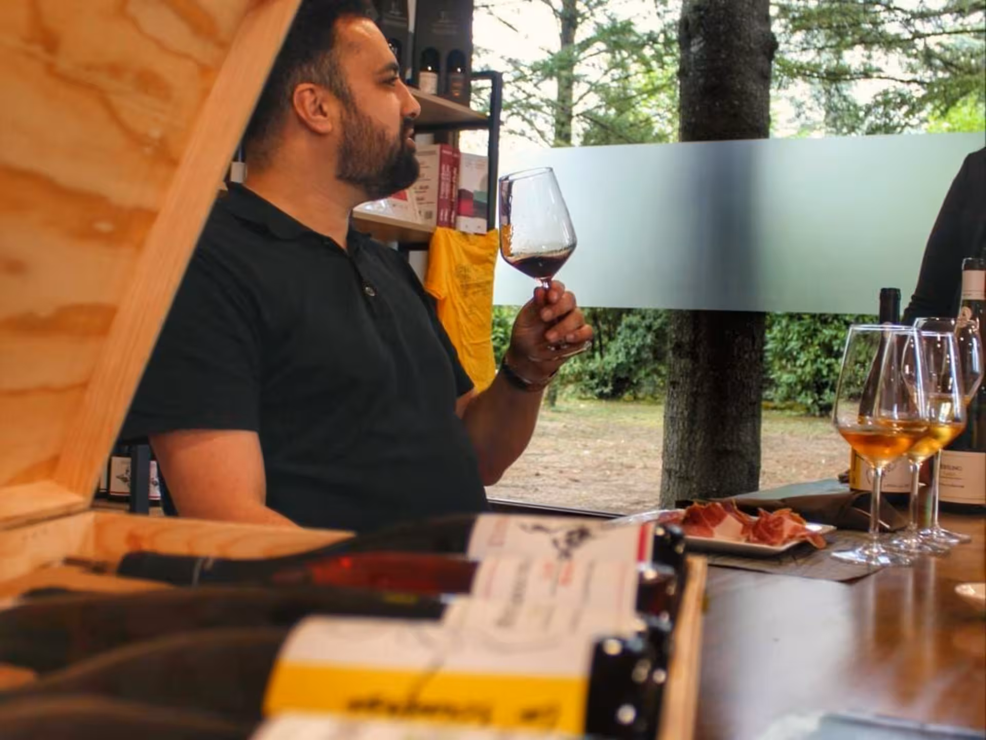 Man enjoying wine tasting at a Rieti countryside winery, with bottles and charcuterie on rustic wooden table.
