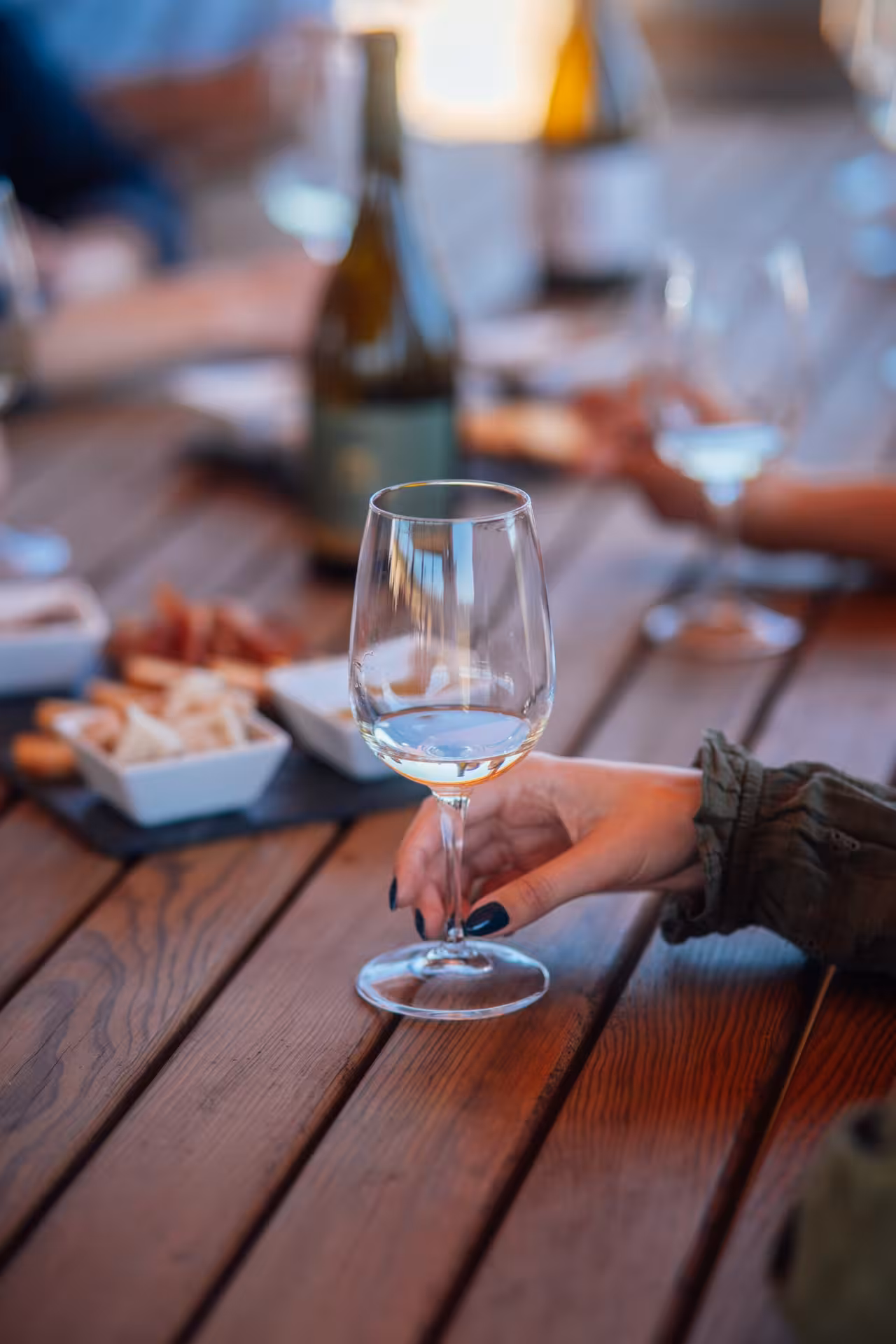 Close-up of white wine glass and snacks on wooden table during Rihla Paxá Visit & Try winery tasting