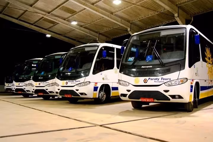 Fleet of Paraty Tours shuttle buses parked under a well-lit terminal, ready for transfers from Rio de Janeiro airports.