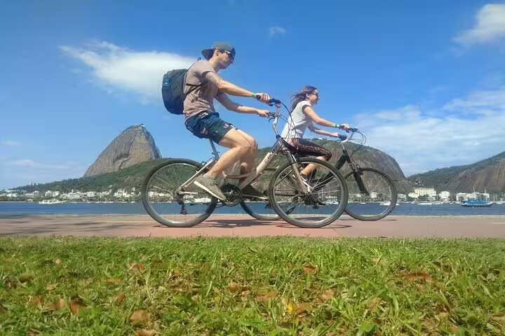 Cyclists enjoying a scenic ride along Rio's coastline with iconic Sugarloaf Mountain in the background on a sunny day.