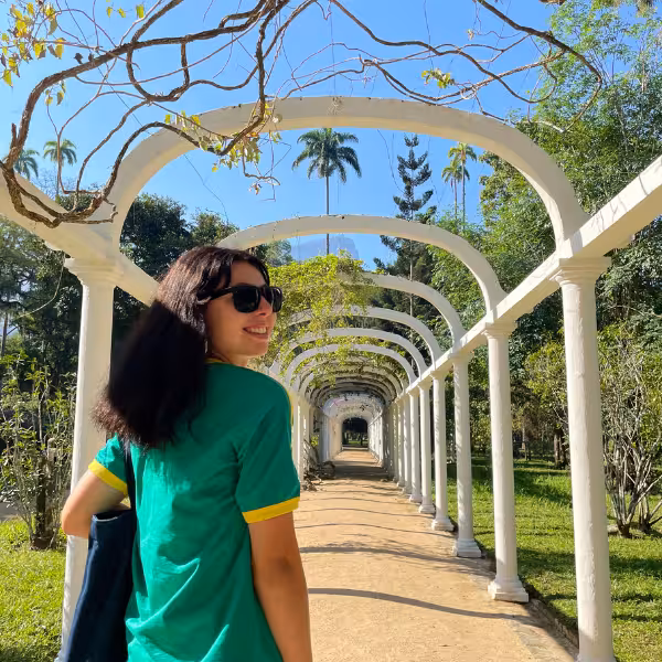 Smiling visitor walking through the picturesque archway in Rio's Botanical Garden, surrounded by tropical plants.