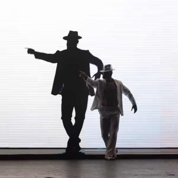 Dancer in white suit with shadowed figure in background at Roxy Copacabana's Rio By Night cultural performance.