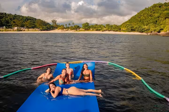 Group lounging on floating mat during private Rio catamaran tour, open bar and beach views with Velas do Rio