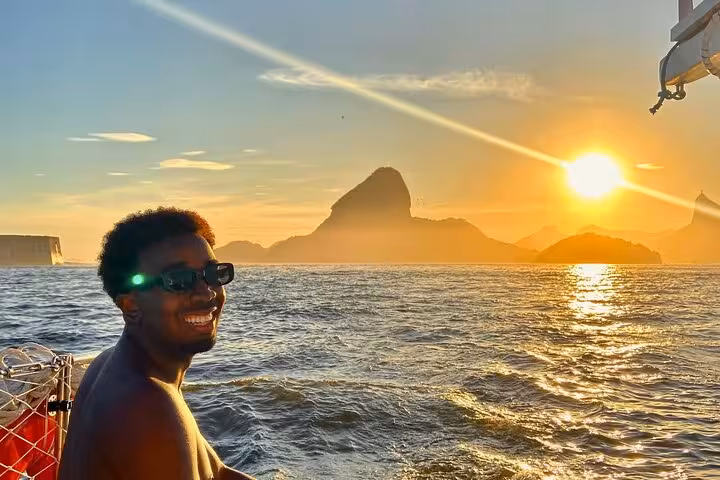 Guest smiling at sunset on Rio catamaran cruise with open bar, ocean views and mountain skyline