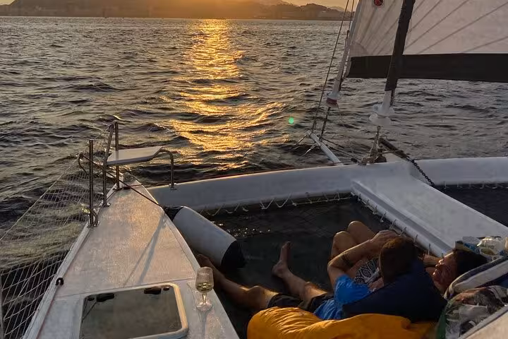 Sunset view from Rio catamaran nets with guests relaxing, 3-hour private sailing tour with open bar Velas do Rio