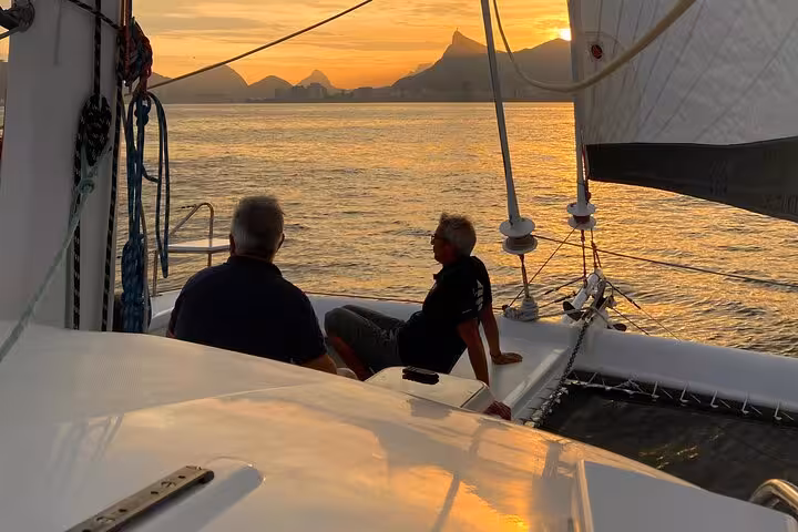 Guests relax on Rio catamaran at sunset with Sugarloaf view on 5-hour sailboat tour with open bar