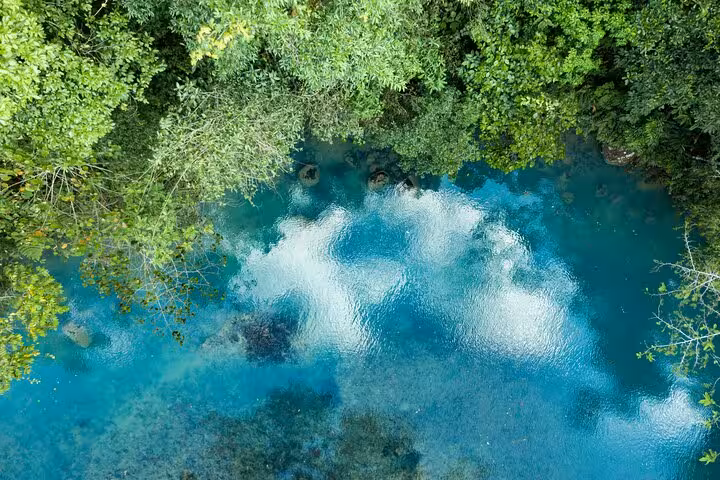 Aerial view of Rio Celeste's striking blue waters reflecting lush forest and clouds, perfect for a scenic nature hike.