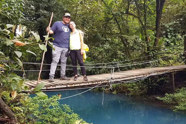 Couple standing on a wooden bridge above Rio Celeste's turquoise waters during a nature hike in Costa Rica's lush rainforest.