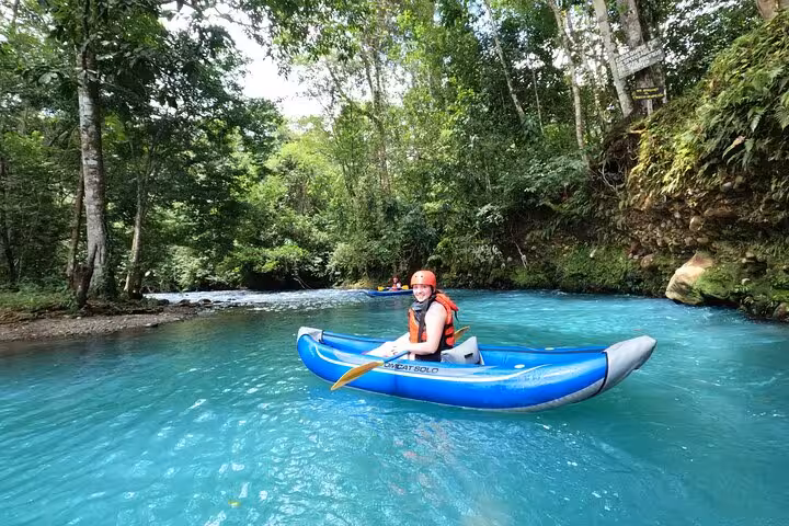 Solo kayaker paddles through the clear blue waters of Río Celeste, exploring the lush Costa Rican jungle.