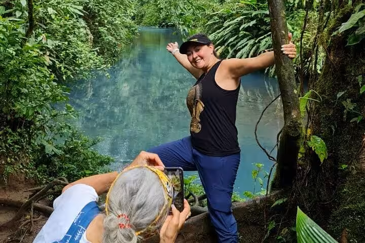 Visitor posing for a photo by the stunning blue waters of Rio Celeste amidst the verdant Costa Rican jungle.