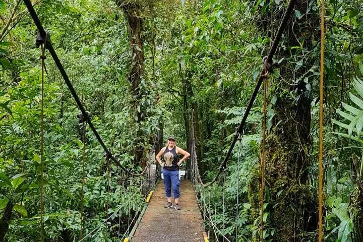 Person standing on a suspension bridge amidst dense green jungle during a Rio Celeste nature hike adventure.