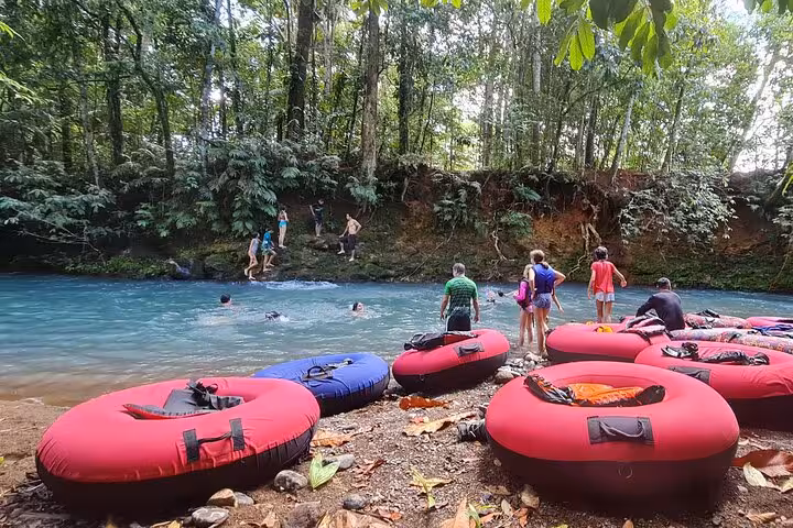 Groups prepare for tubing adventure in Rio Celeste's lush rainforest surrounded by vibrant blue waters.